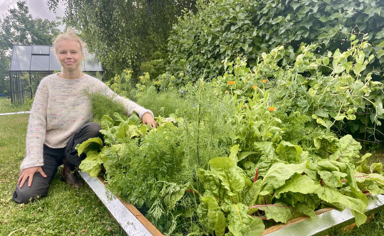 Laura i haven mellem frodige bede — varmt lys, planter i forgrunden